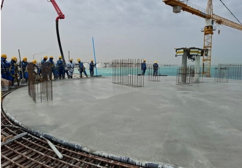 Daytime aerial view of workers around rebar column starters with a crane and coastline