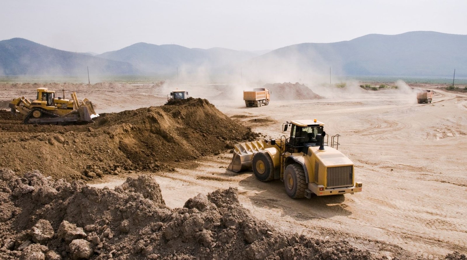 Bulldozer, wheel loader, and dump trucks moving earth on an active site