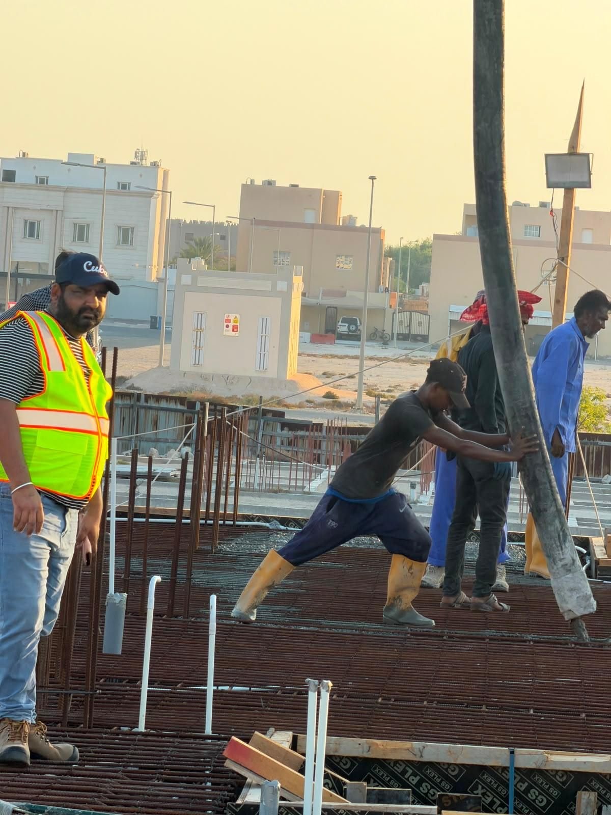 Fareeq Al Suroor crew guiding a concrete pump hose during a slab pour, golden hour