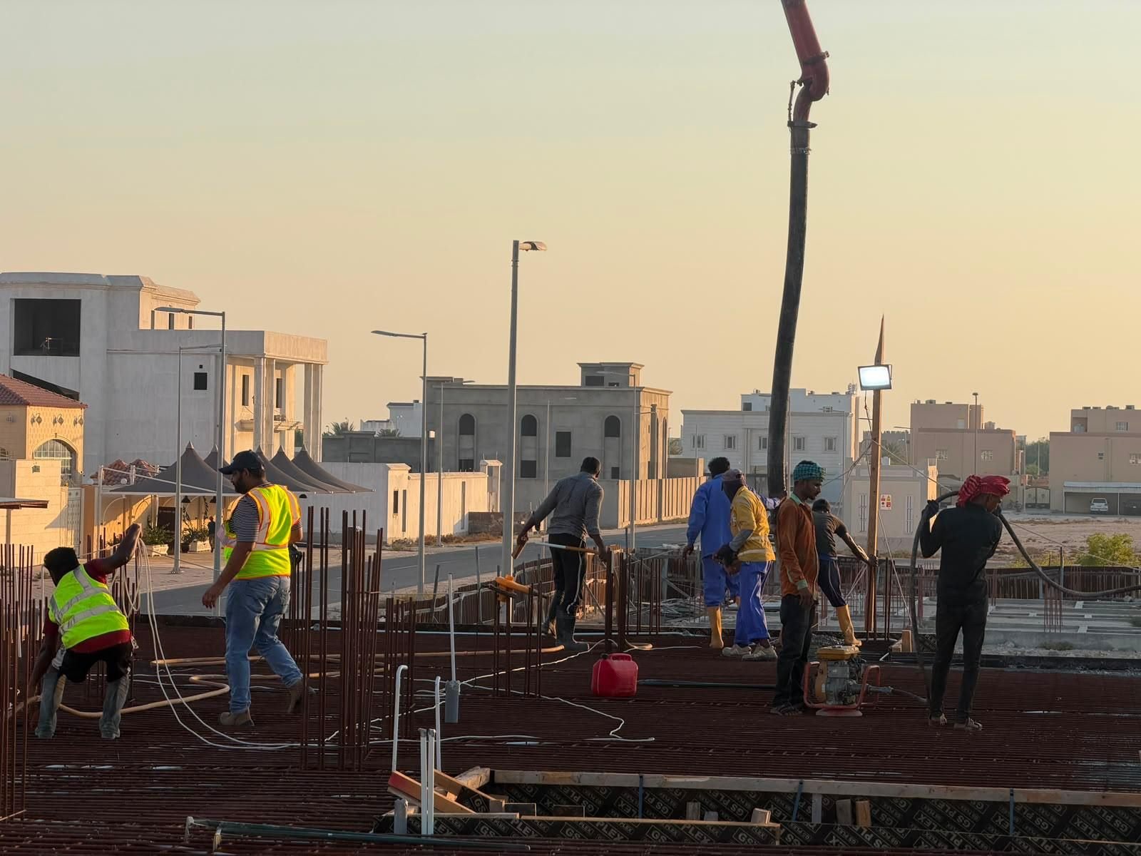 Fareeq Al Suroor site team and concrete pump boom at a Doha construction site, golden hour